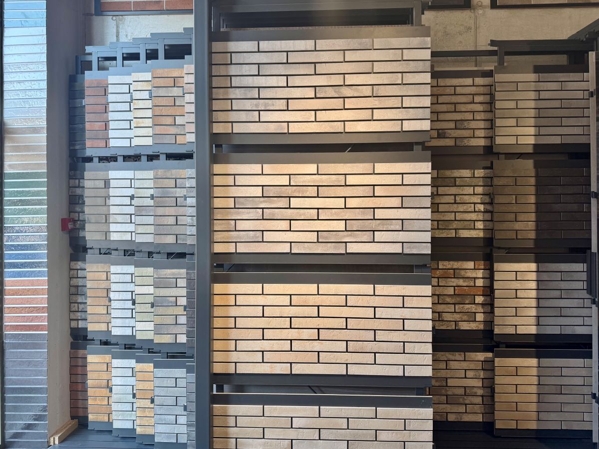 Brick sample display in a showroom with beige, gray, and brown brick panels arranged on metal racks on multiple shelves.