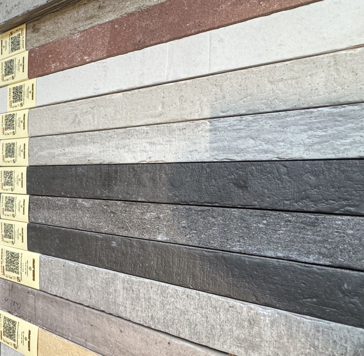 Row of horizontal wall panels in gray to charcoal tones with yellow price tags along the left edge.