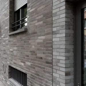 Brick exterior of a building with a barred window and a metal security shutter above it, seen at an angle alongside a door frame on the right