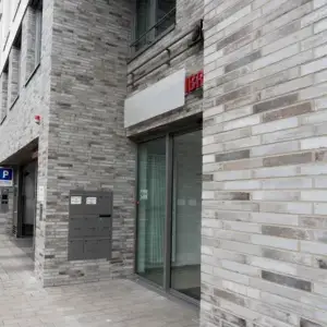Facade of a modern brick building with a glass entrance and row of mailboxes, gray stone bricks, and a red IBR sign.