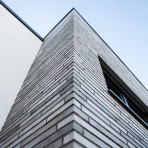 Corner view of a brick building rising against a clear blue sky, photographed from a low angle showcasing sharp geometric lines and brick pattern outward.