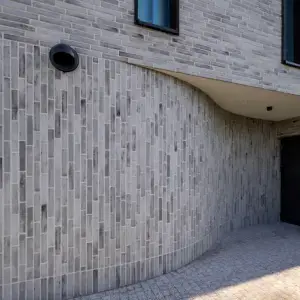Curved light-gray brick wall of a modern building with a black round vent and a dark door at right under a beige overhang