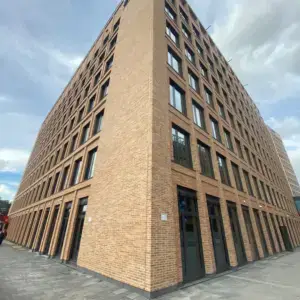 Brick office building seen from a low-angle corner, rows of large windows under a pale blue sky.